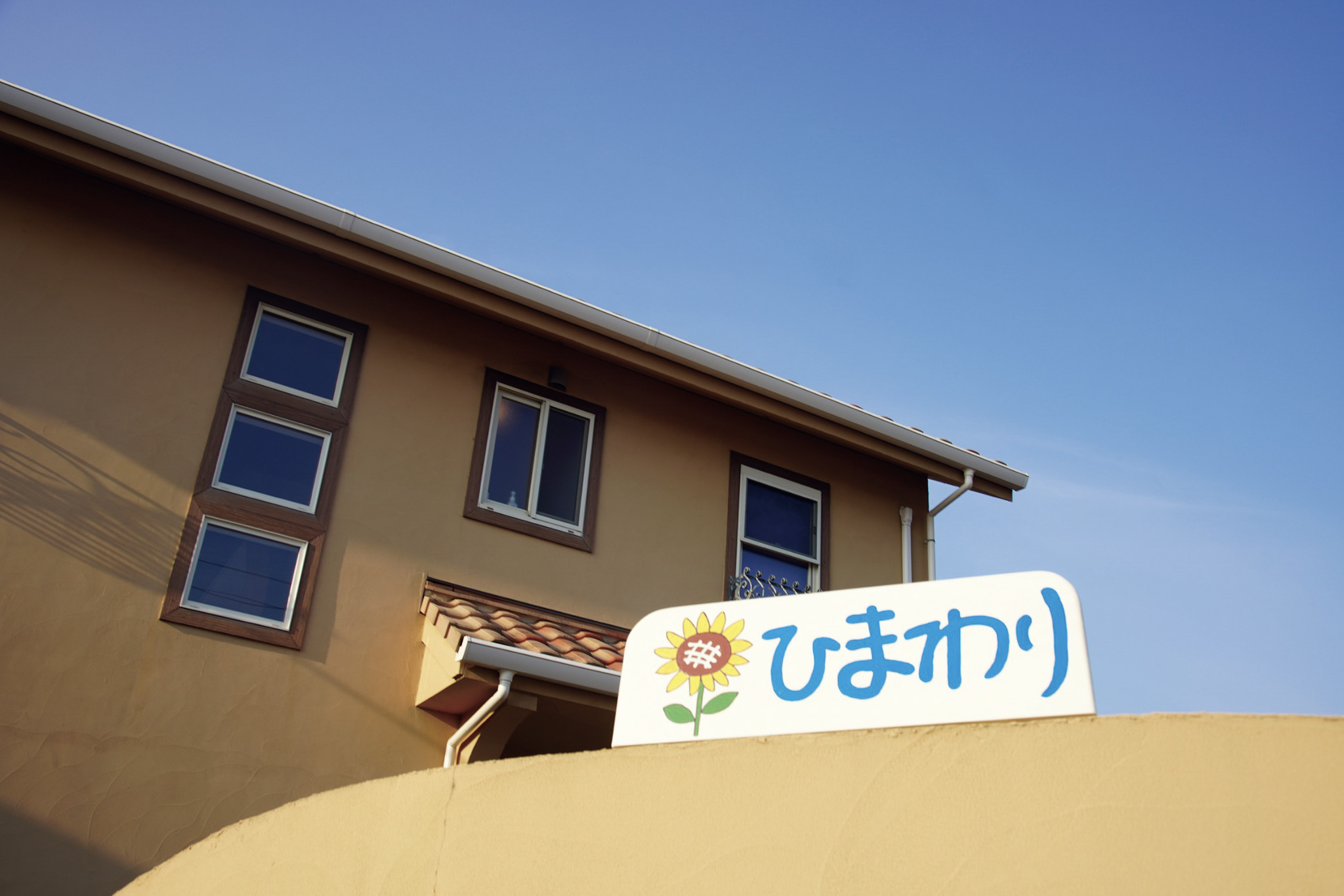 青空を背景にした、ひまわりの看板がある家